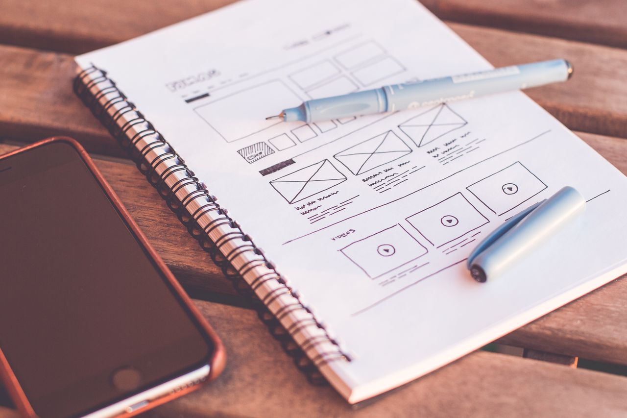 Home Close-up of a notebook with wireframe sketches and a smartphone on a wooden desk.